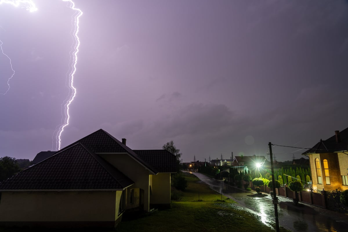 Lightning storm illuminating a residential neighborhood at night during a power outage — the exact scenario a Generac whole-home generator protects against